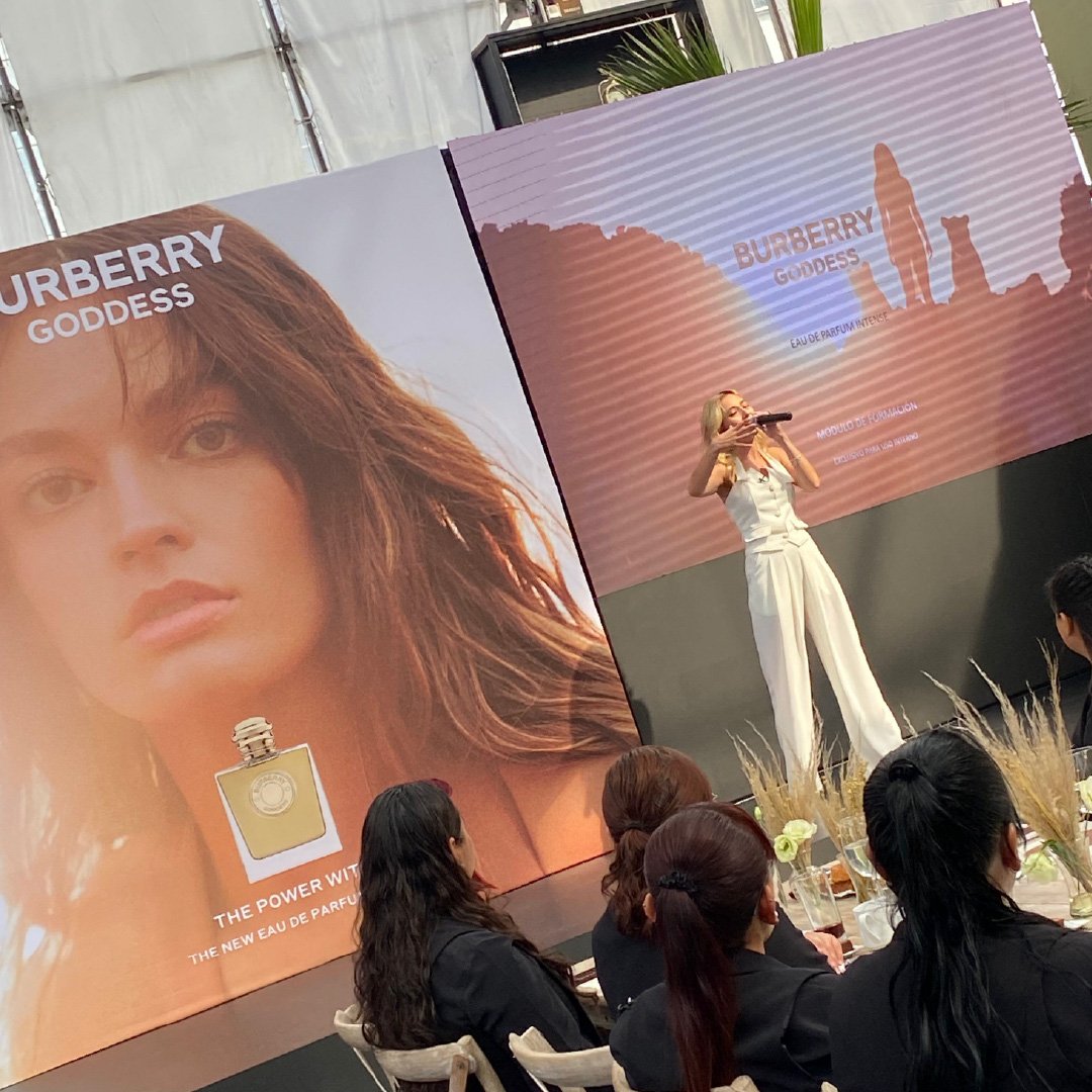 Una mujer en un escenario presentando el perfume Burberry Goddess frente a una audiencia.