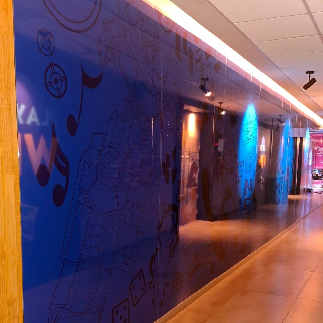 Pared azul con dibujos y juegos de palabras en letras negras, en un pasillo con iluminación cálida y entorno moderno.