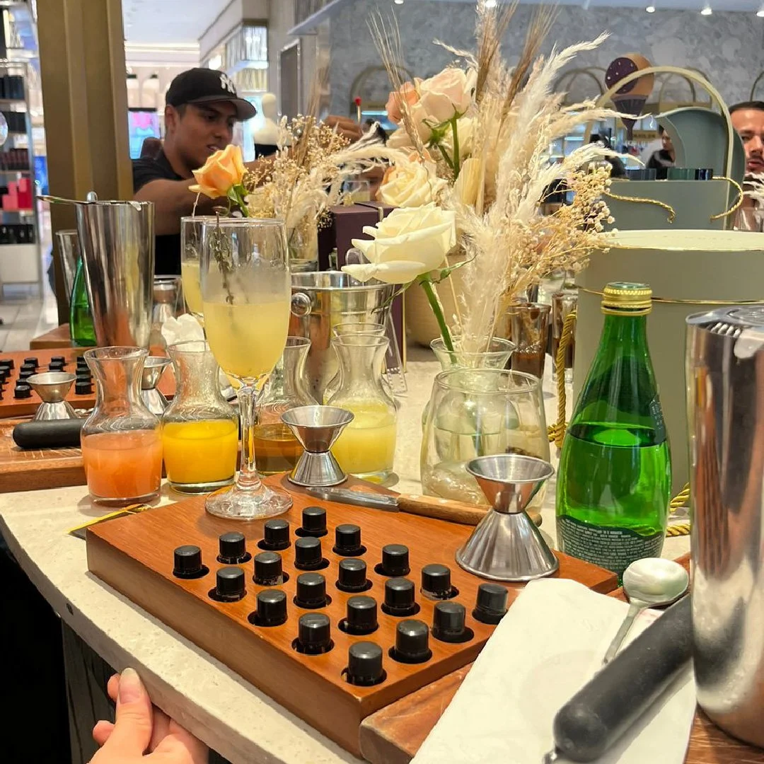 Conjunto de ingredientes y utensilios para preparar cócteles en una mesa decorada con flores en un establecimiento.