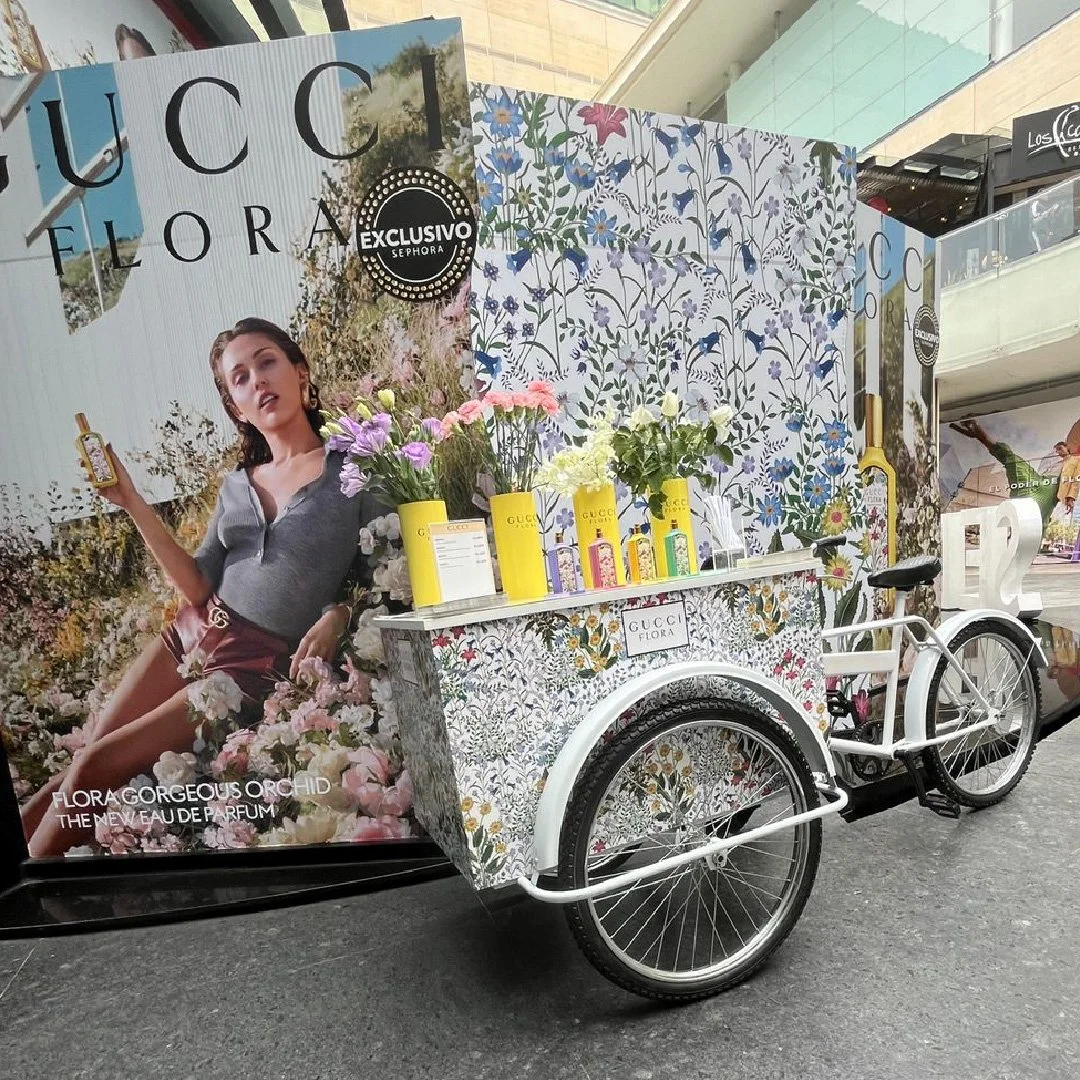 Carro de carga decorado con flores y publicidad de la marca Gucci y perfumera, con un cartel que dice 'Flora Gorgeous Orchid'