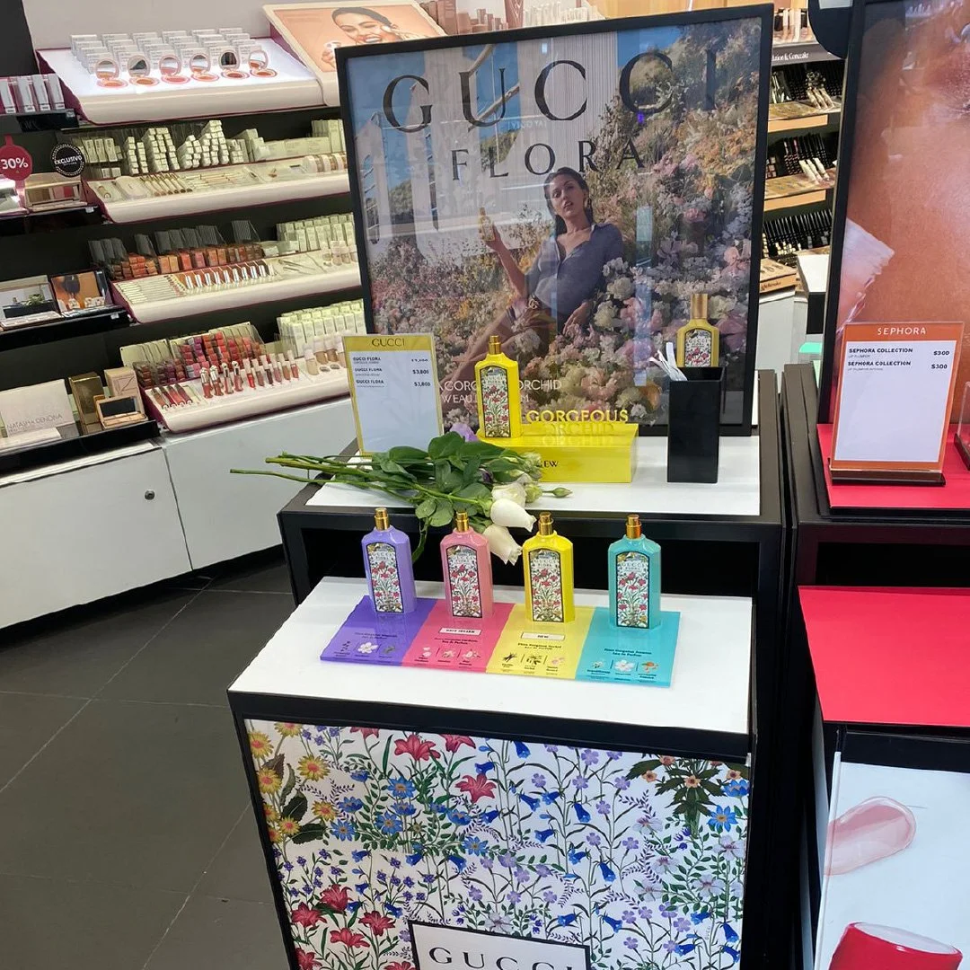 Exhibición de perfumes Gucci con envases coloridos y flores blancas en una tienda de maquillaje. LVMH Activacion punto de venta