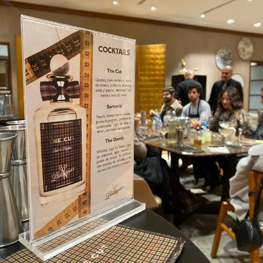 Menú de cocteles en un restaurante, con tres bebidas listadas y una imagen de una botella de licor y un medidor de alcohol en la portada.