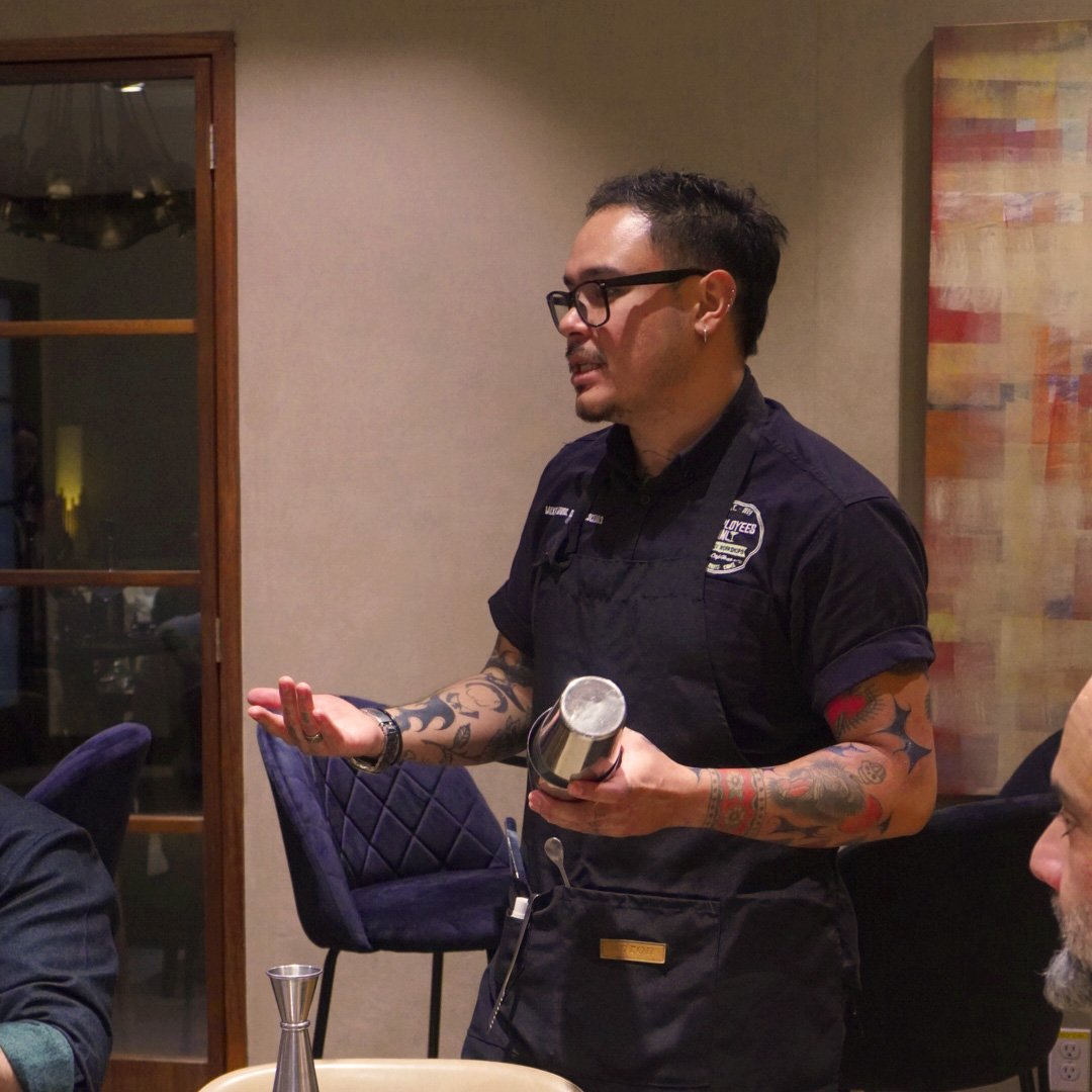 Hombre con gafas y tatuajes sirviendo una bebida en un restaurante o cafetería.