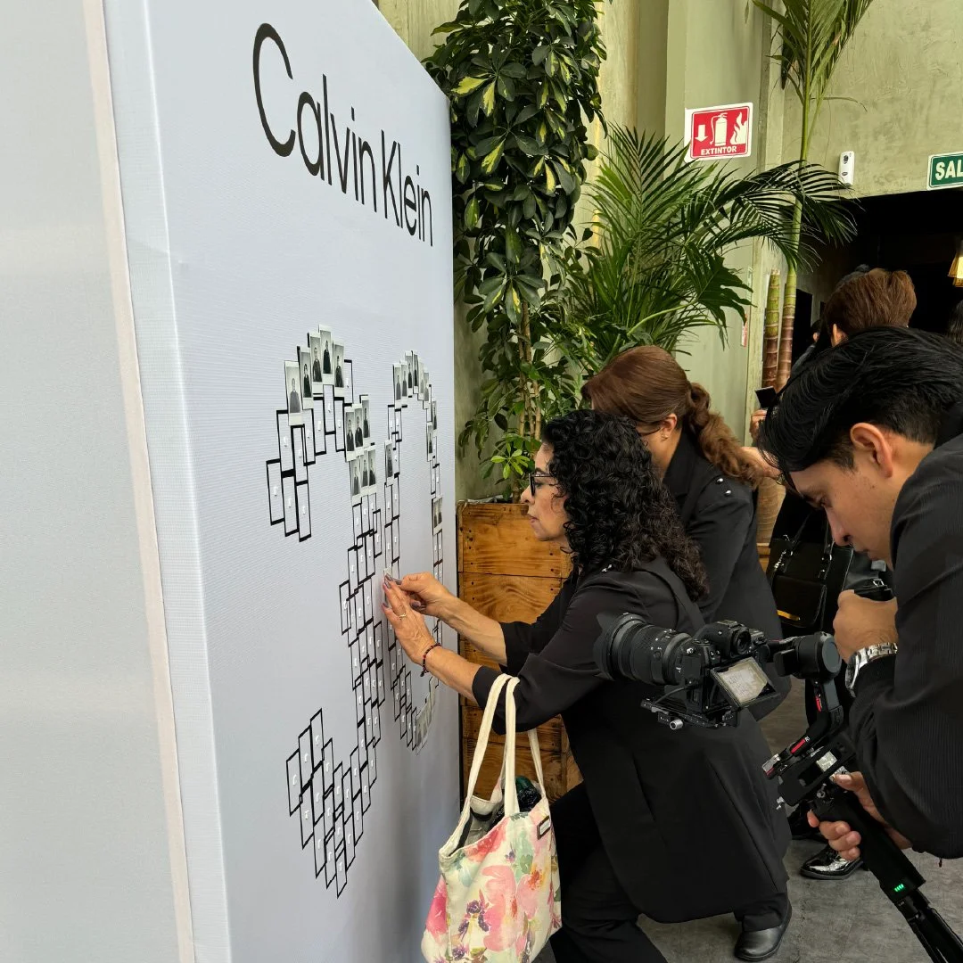 Personas en blanco y negro colocando fotografías en un cuadro en forma de árbol en una pared