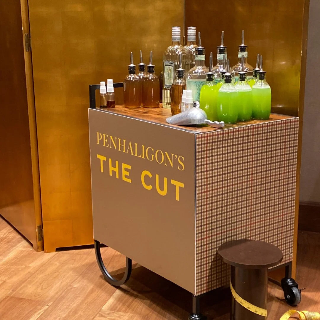 Carrito de barra con varias botellas de alcohol y líquidos de diferentes colores, en el establecimiento 'Penhaligon's The Cut'. Ahí hay un pequeño banco y una cinta métrica.