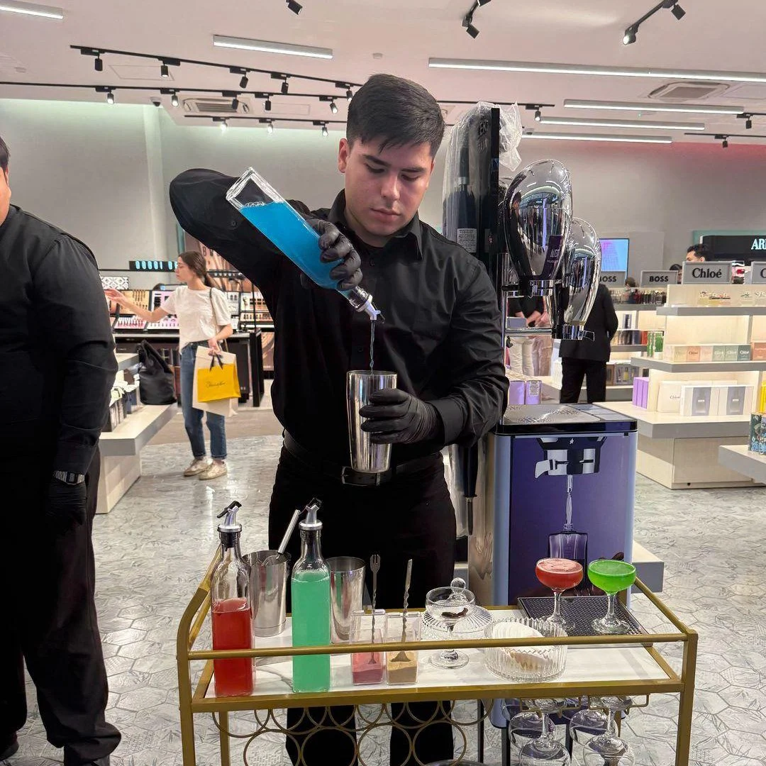 Un bartender mezclando bebidas coloridas en un bar, en una tienda de perfumes. Activacion punto de ventan franslux