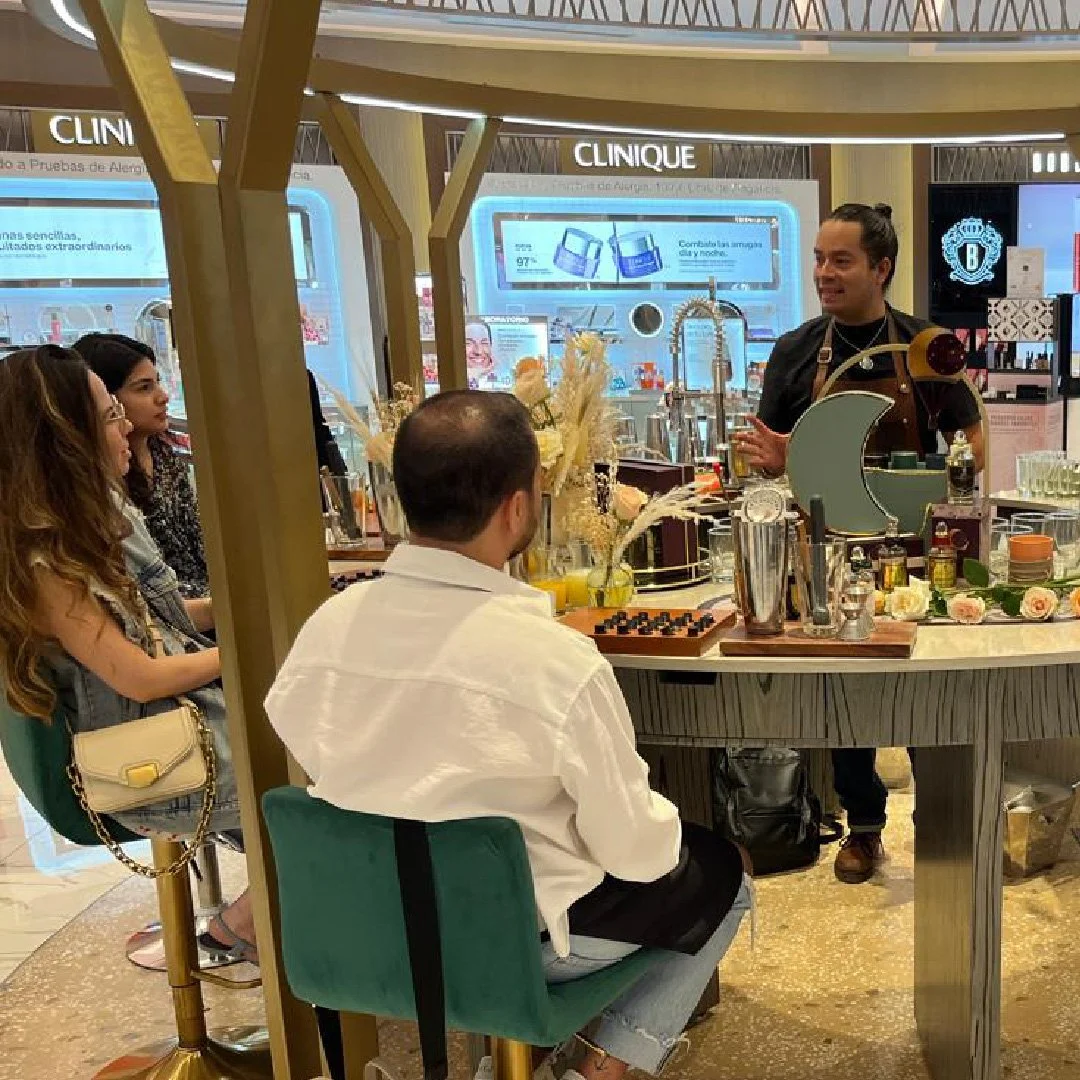 Un grupo de personas participando en una clase de coctelería en un espacio decorado con flores. Un instructor explica mientras otros observan.