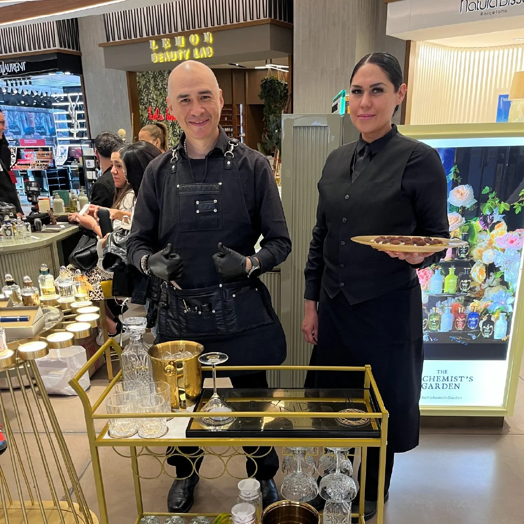 Dos personas, un hombre y una mujer, en un escaparate de una tienda de belleza. La mujer sostiene un plato.