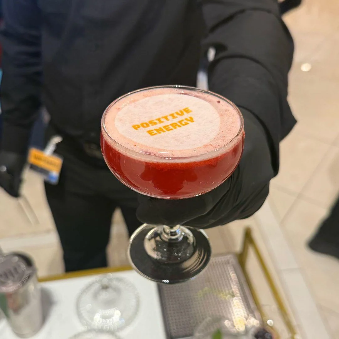 Cóctel rosa en copa de cóctel con la frase 'Positive Energy' en la superficie.