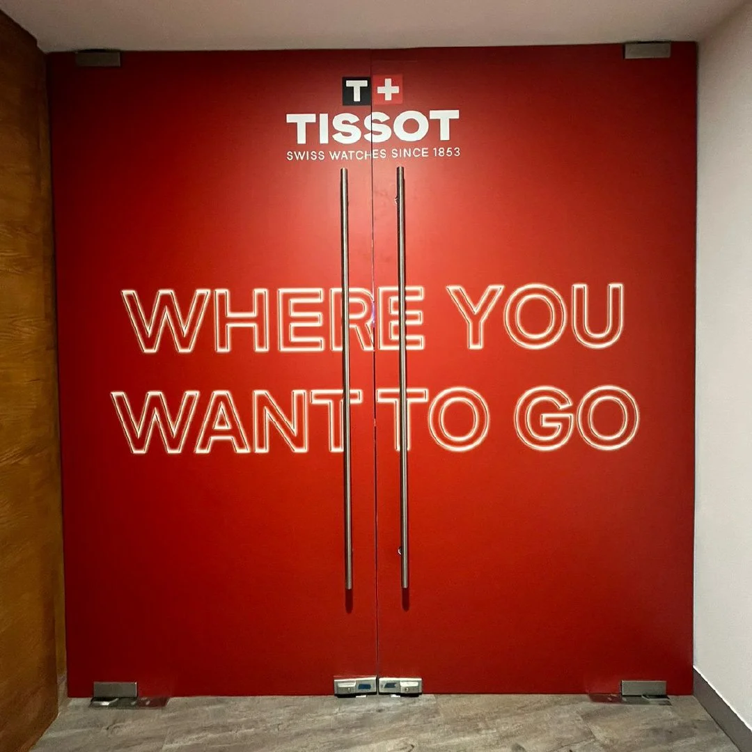 Puertas rojas con letras de neón blancas que dicen 'Where you want to go', logotipo de Tissot y lema 'Swiss watches since 1853'. Tissot training