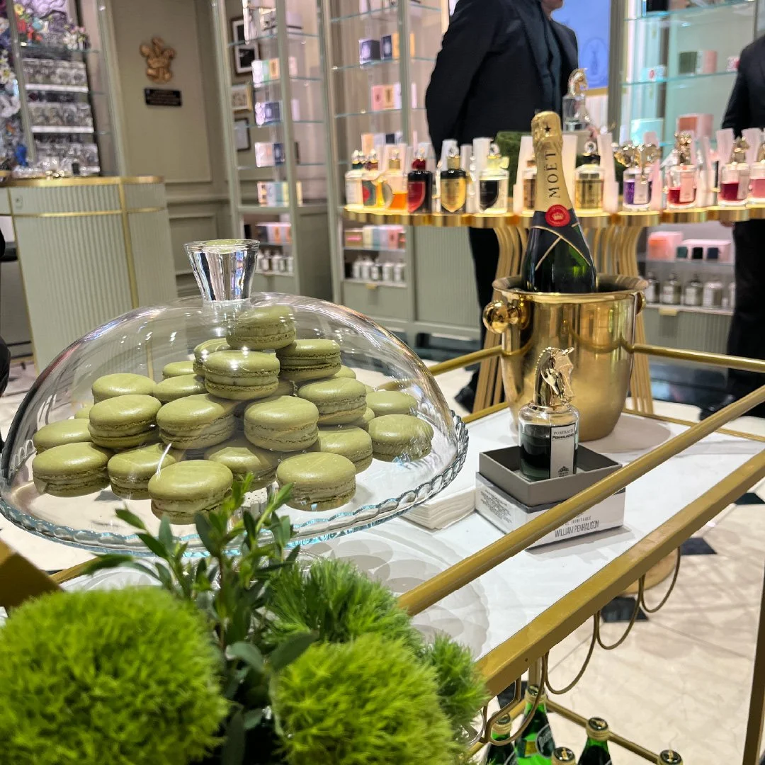 Macarons verdes en una bandeja de servir de vidrio en una mesa decorada con plantas verdes y una botella de champagne en un recipiente dorado.