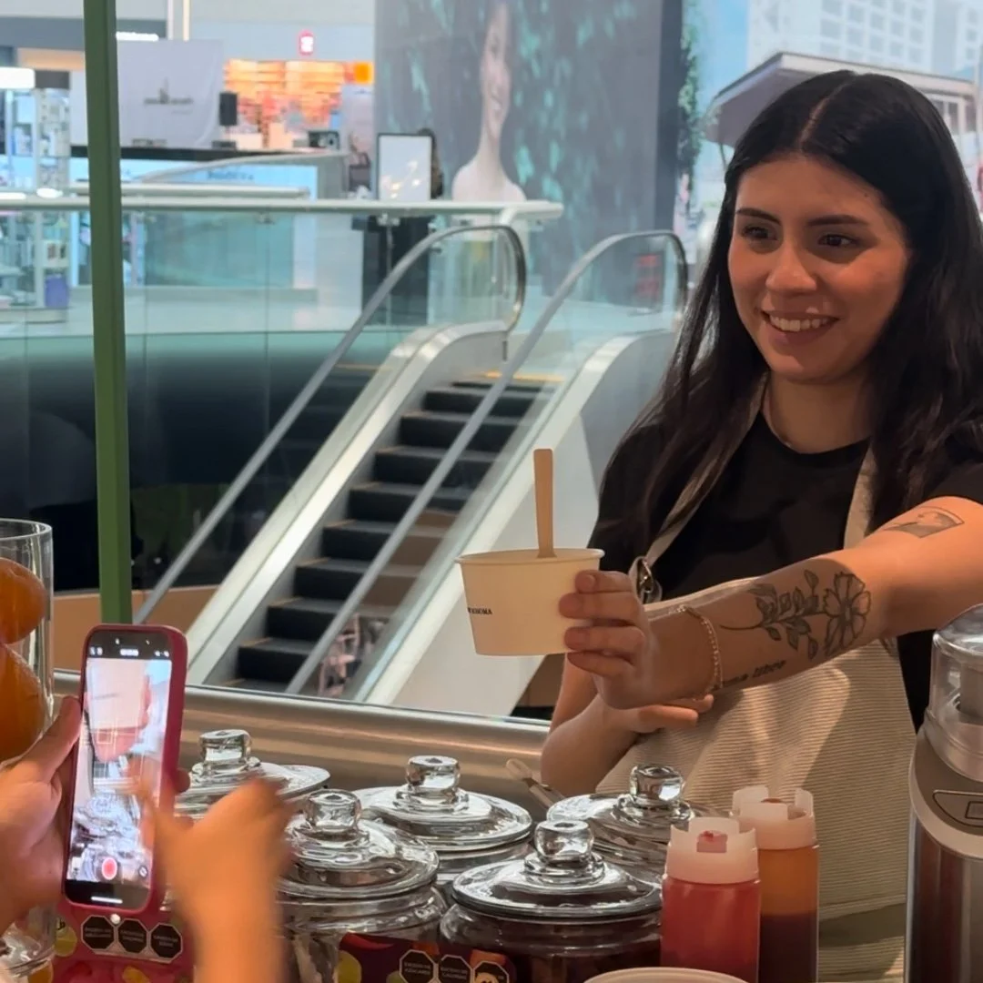 Una mujer sonriendo recibe un helado en una tienda, mientras alguien toma una foto con un teléfono móvil.
