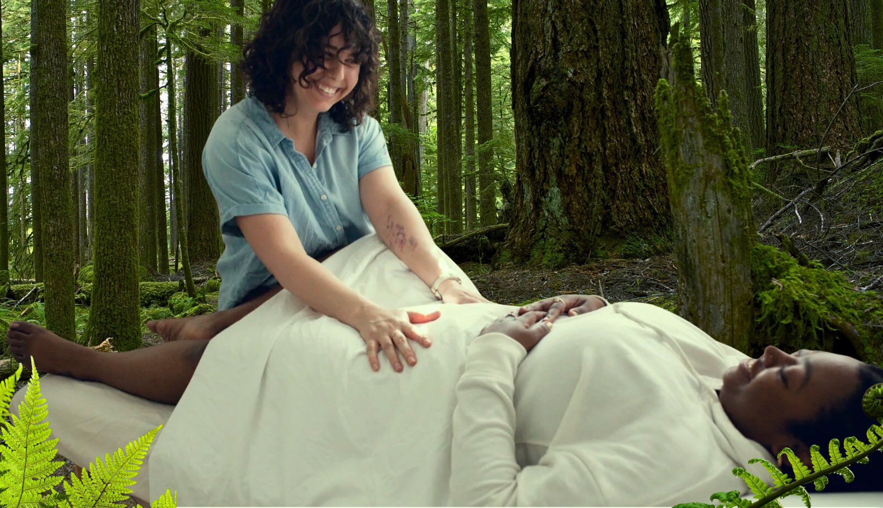 Dr. Grace (White, brown curly hair,) in a blue, short-sleeved shirt, with hands gently reaching out and resting on the pelvis of a client. The client (Black woman) lying rested and comfortable on the table. They are both smiling.