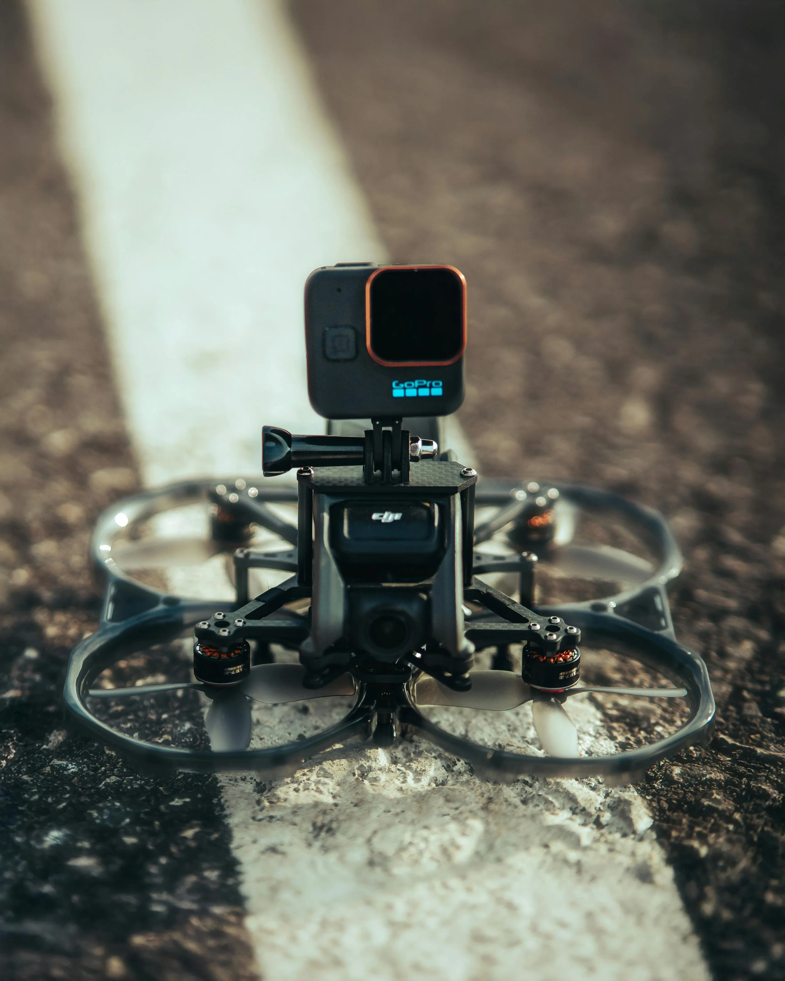 A drone with a mounted GoPro camera on a flat asphalt surface.