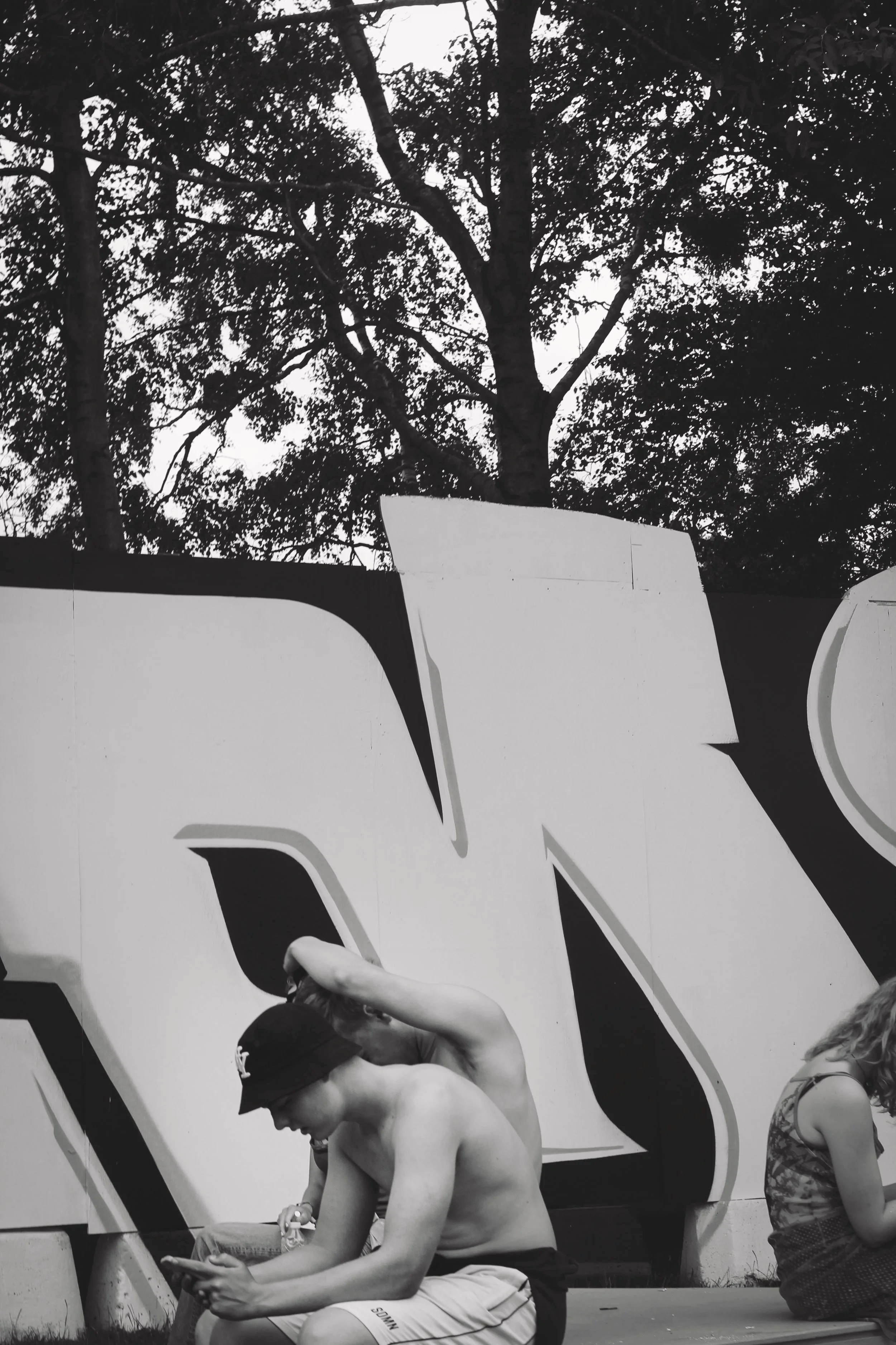 Sort-hvid fotografi af unge mennesker, der sidder foran store bogstaver i et urbant byrum på Roskilde Festival