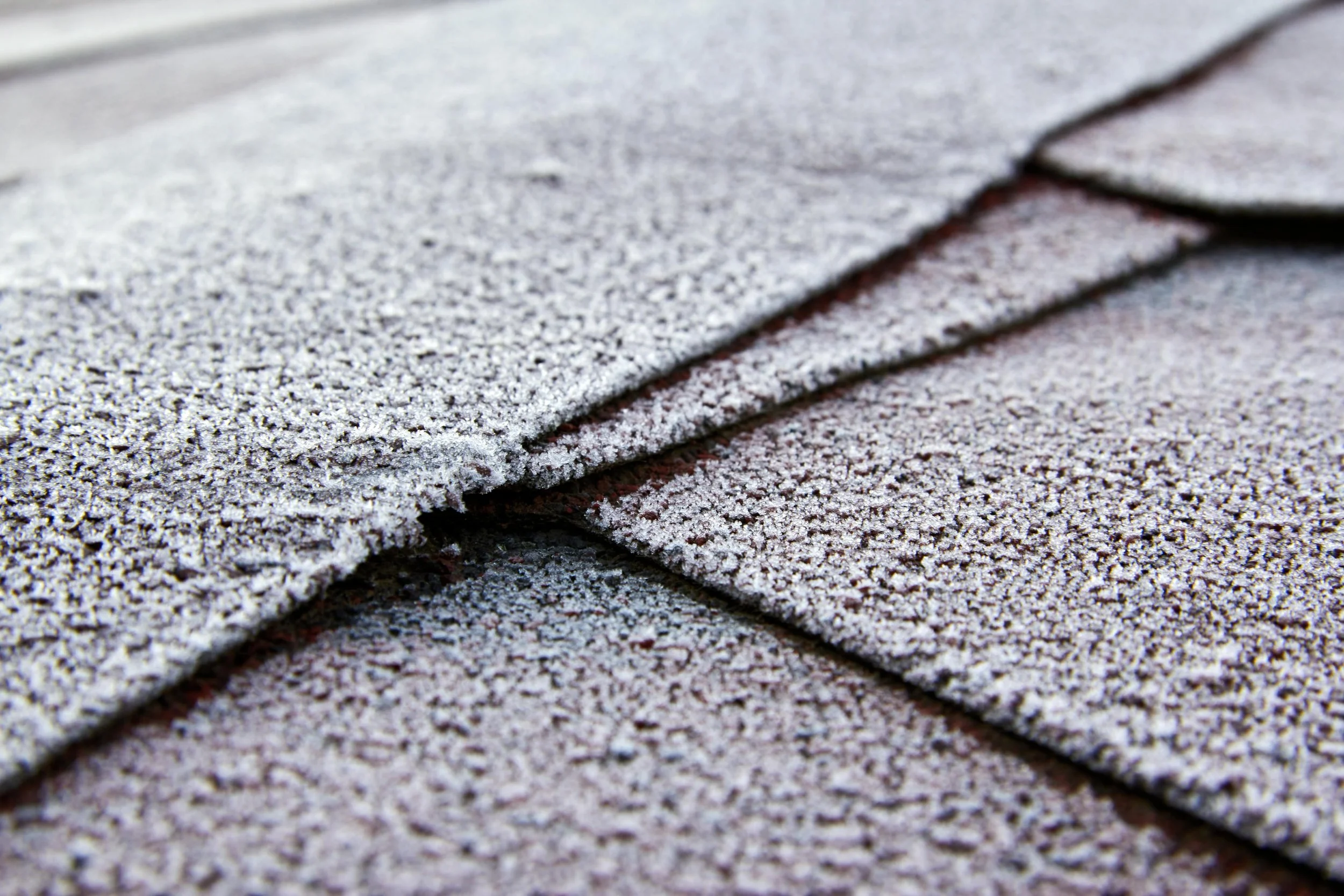 Close-up of textured roofing shingles with frost or snow on surface.