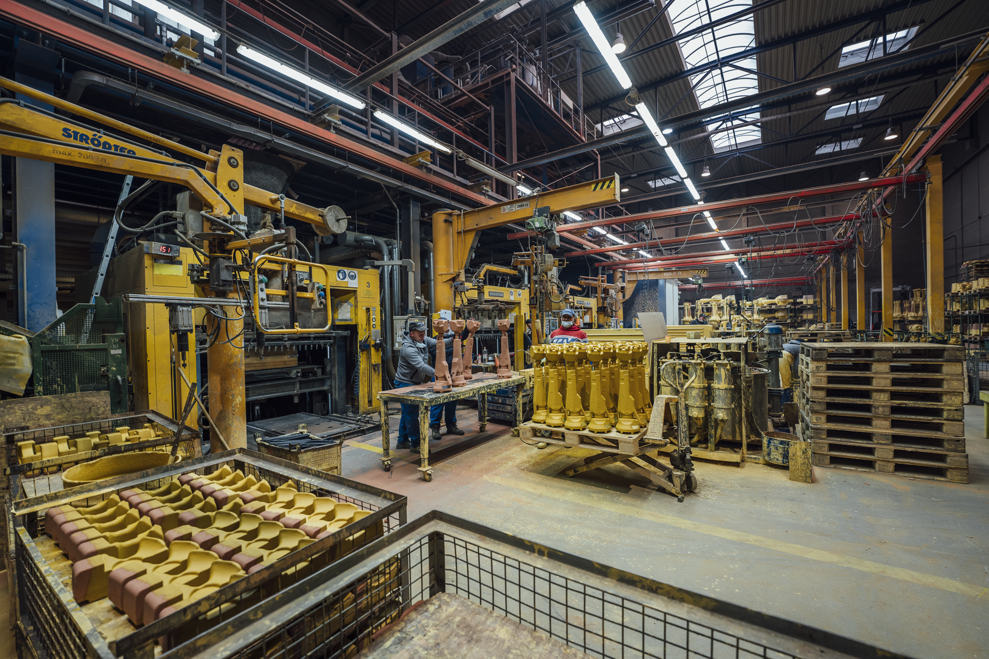 Industrielle Fertigungshalle mit Maschinen und Arbeitern bei der Produktion, viele gelbe Bauteile auf Paletten, industrielle Ausrüstung, kontrollierende Arbeiter