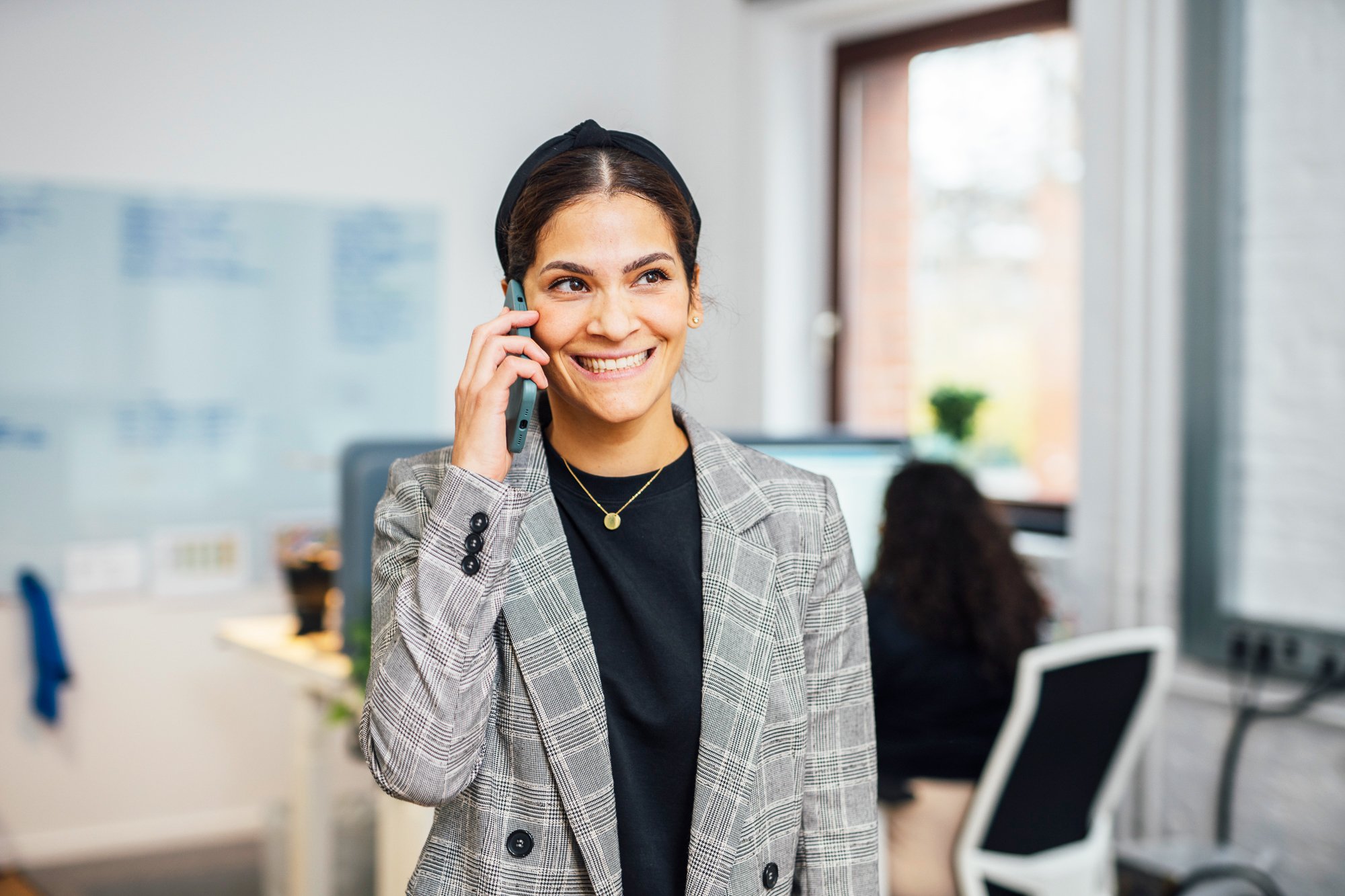 Junge Frau im Büro spricht am Telefon und lächelt.
