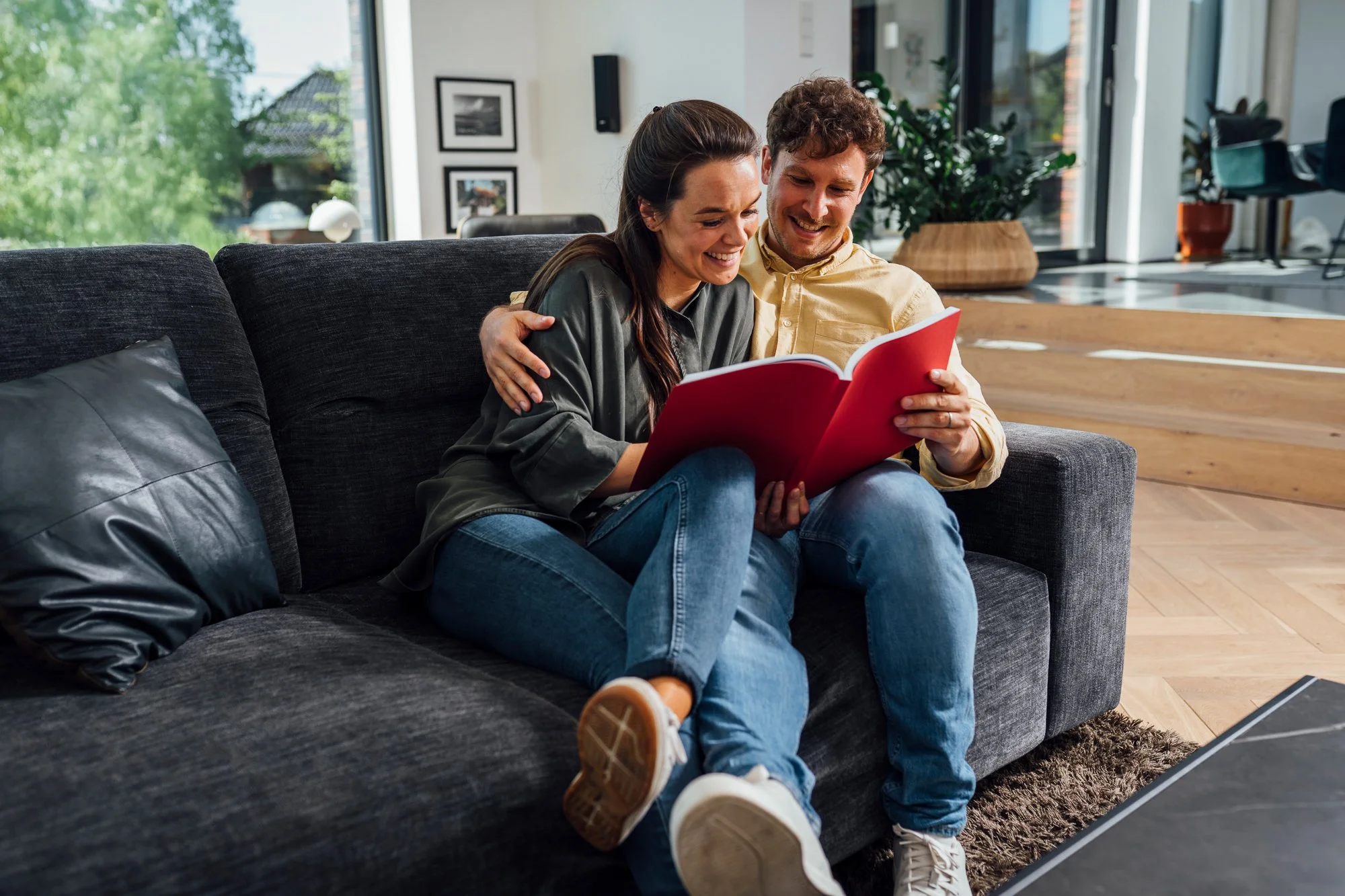 Ein glückliches Paar sitzt auf einem dunklen Sofa und schaut sich zusammen ein Fotoalbum an.