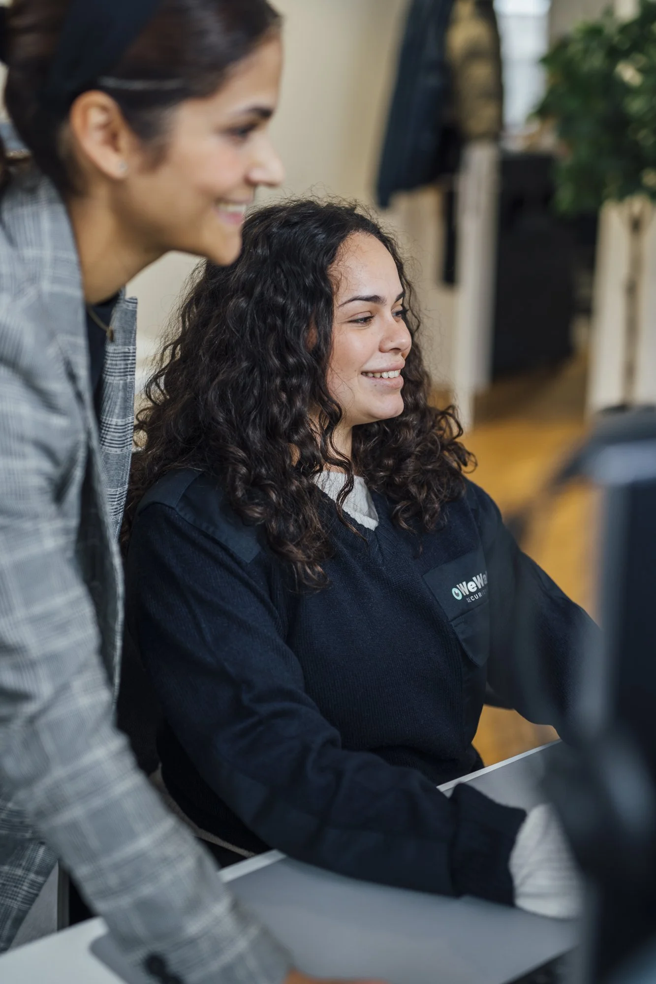 Zwei Frauen schauen gemeinsam auf einen Computerbildschirm, beide lächeln.