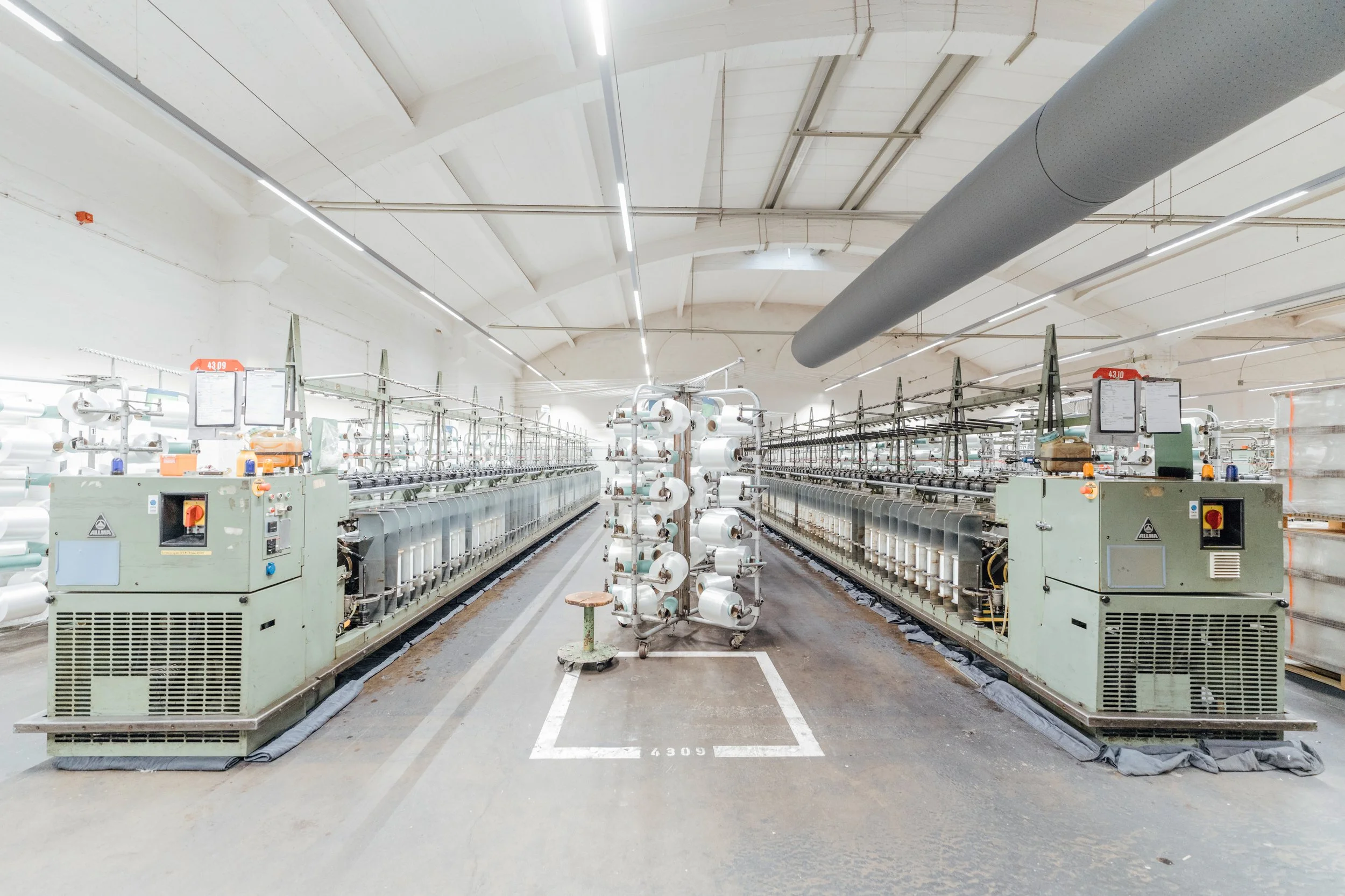 Innenansicht einer Textilfabrik mit großen Maschinen und Spulen in der Mitte.