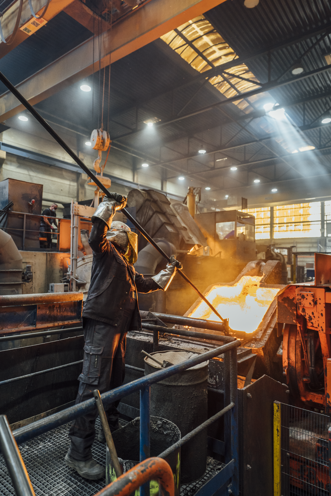 Ein Industriemitarbeiter in Schutzkleidung arbeitet in einer metallverarbeitenden Fabrik, mit heißem flüssigem Metall, das in eine Form gegossen wird.