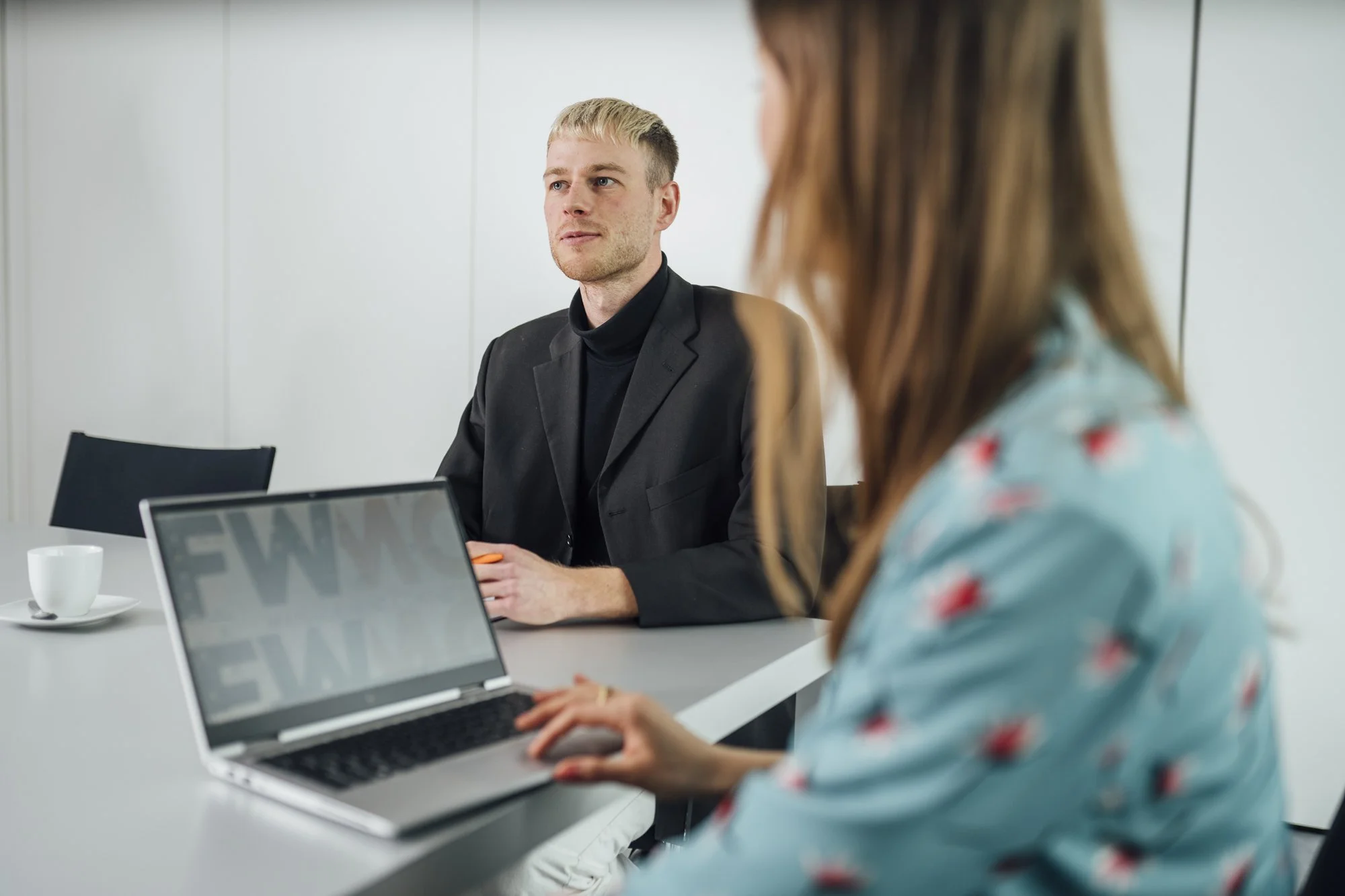 Zwei Menschen bei einem Meeting in einem modernen Konferenzraum, einer mit Laptop, der andere mit einem Smartphone, beide professionell gekleidet.