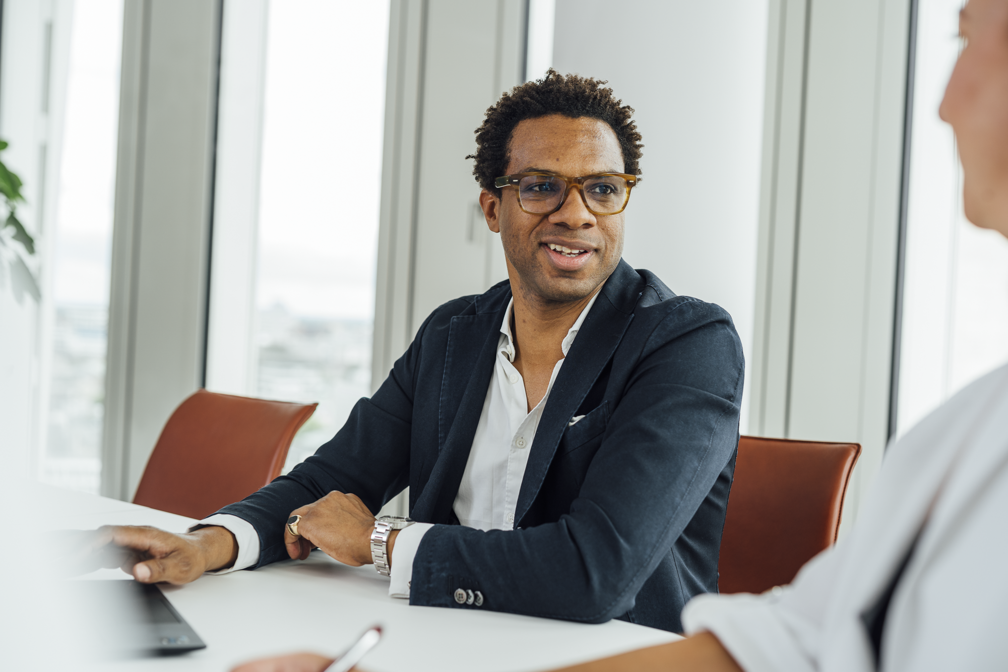 Mann in Brille und dunklem Anzug im Gespräch mit einer Frau in Weiß in einem modernen Büro.
