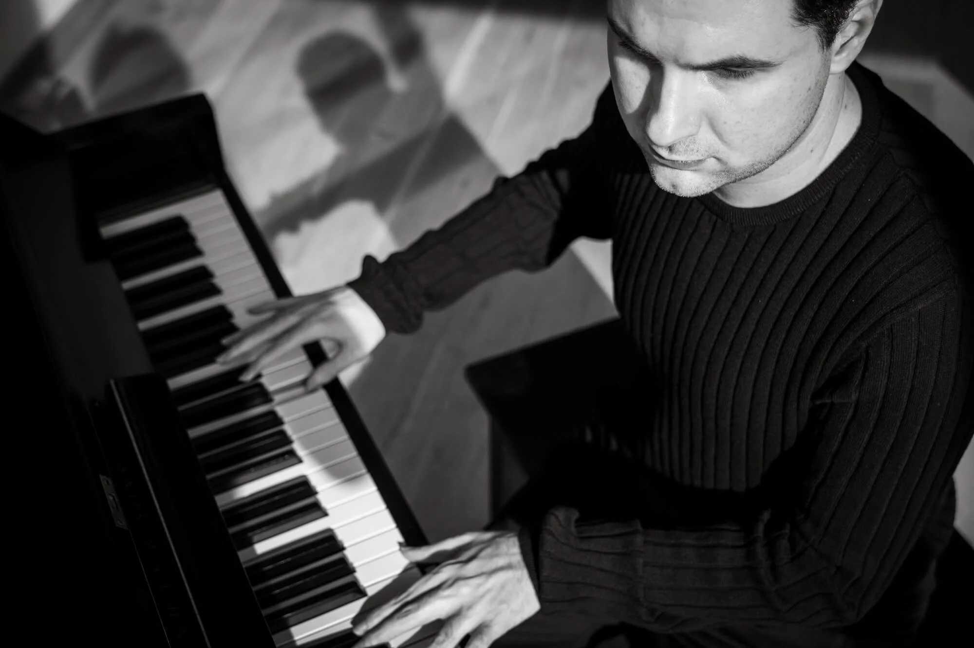 A young man playing a piano, shot from above, in black and white.