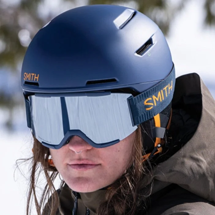 Close-up of a person wearing a blue ski helmet and ski goggles outdoors.