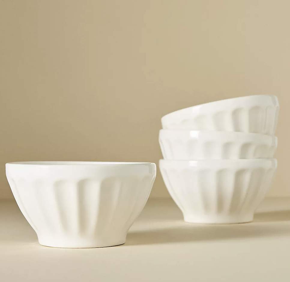 Four white ceramic bowls with fluted sides, one in the foreground and three stacked in the background.