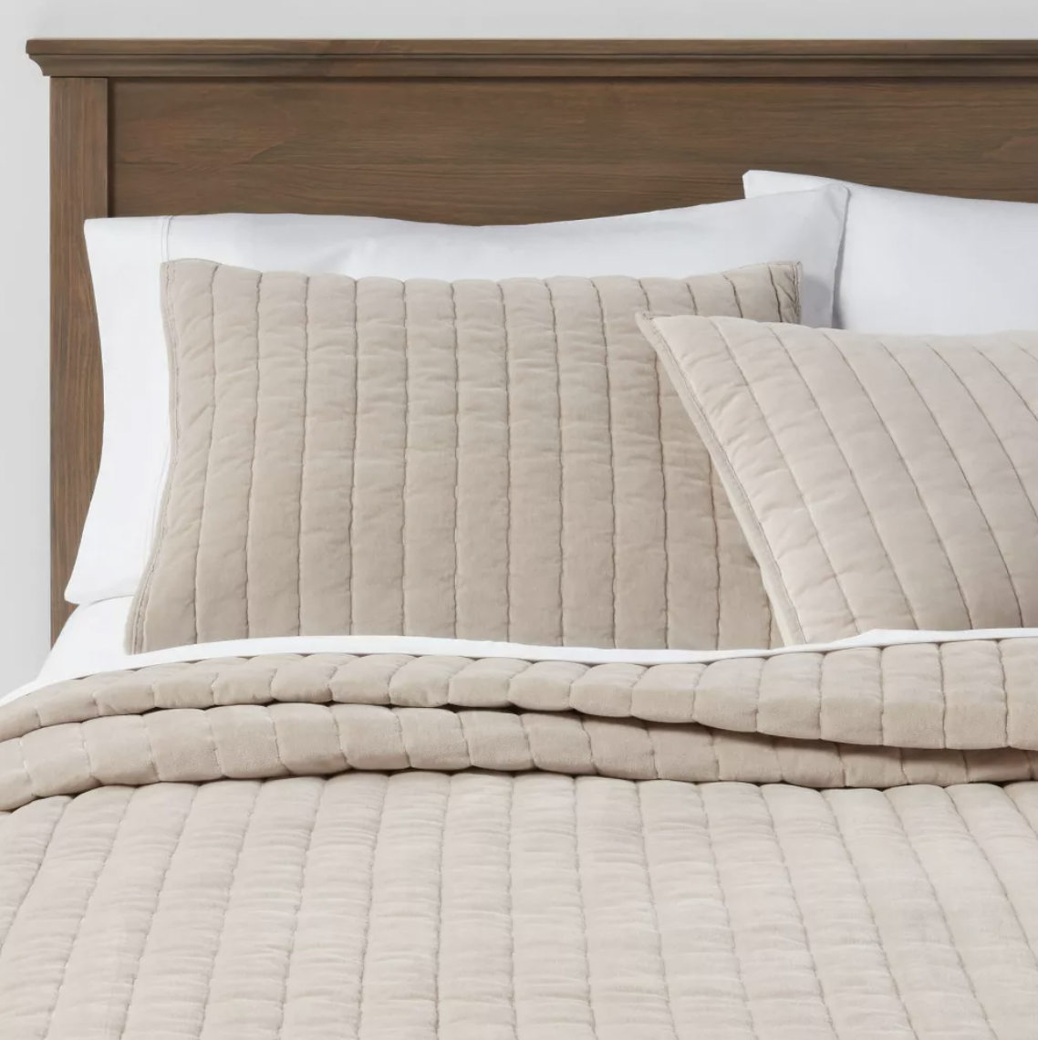 Close-up of neatly made bed with beige quilted pillows and a beige blanket, against a wooden headboard.