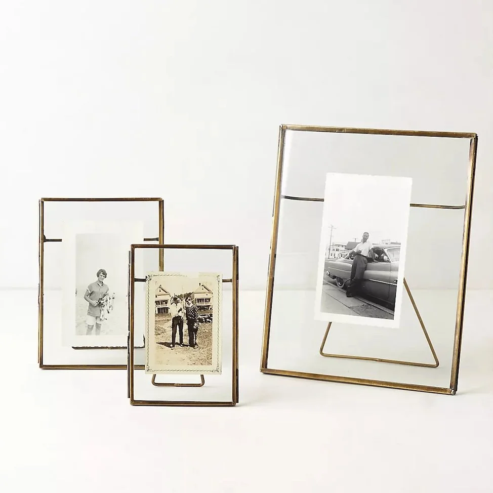Group of four vintage photo frames with black and white photographs inside, set against a plain white background. The frames are in various sizes and styles, with the largest frame on the right side leaning back slightly.