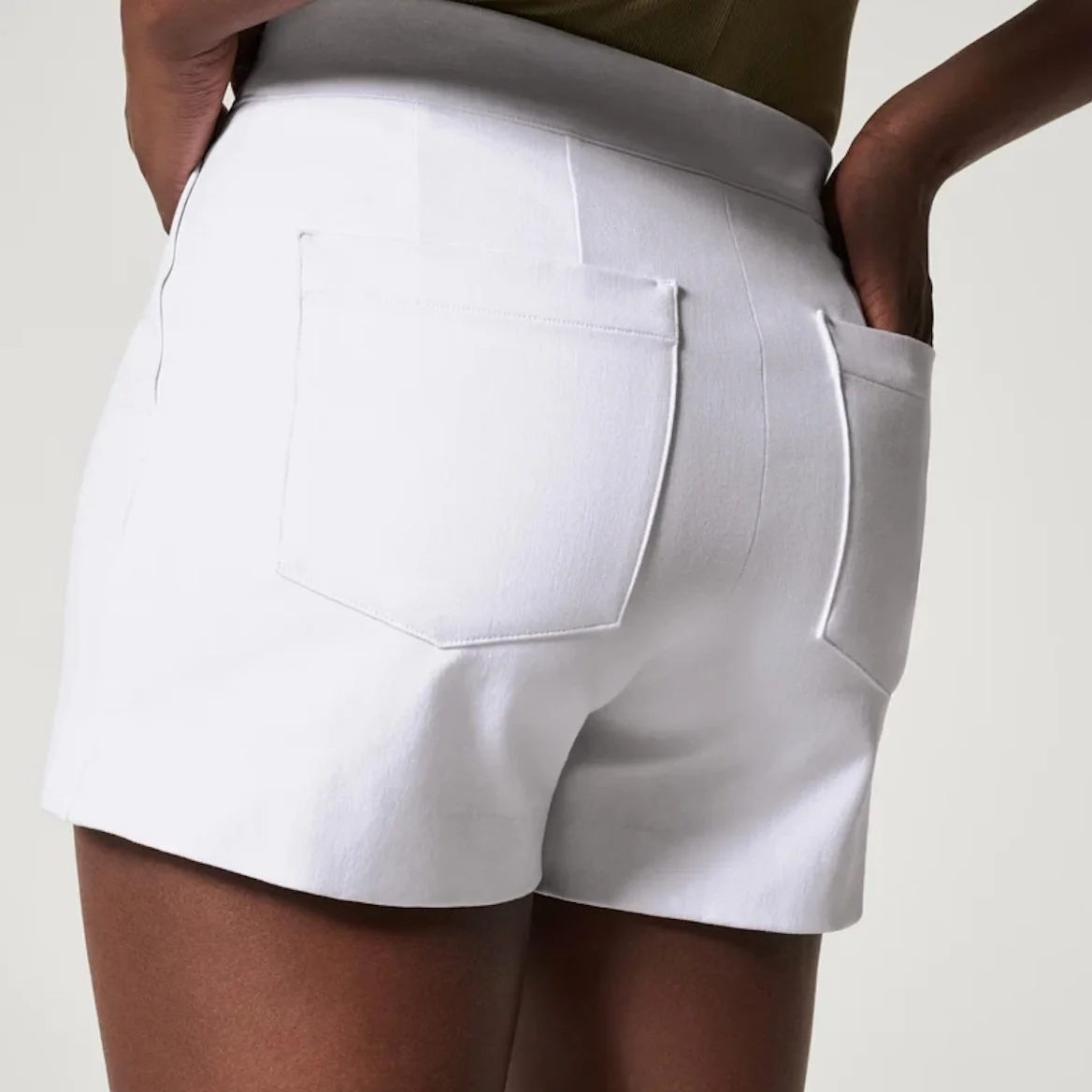 Close-up of a person wearing white high-waisted shorts with their hand in the back pocket.