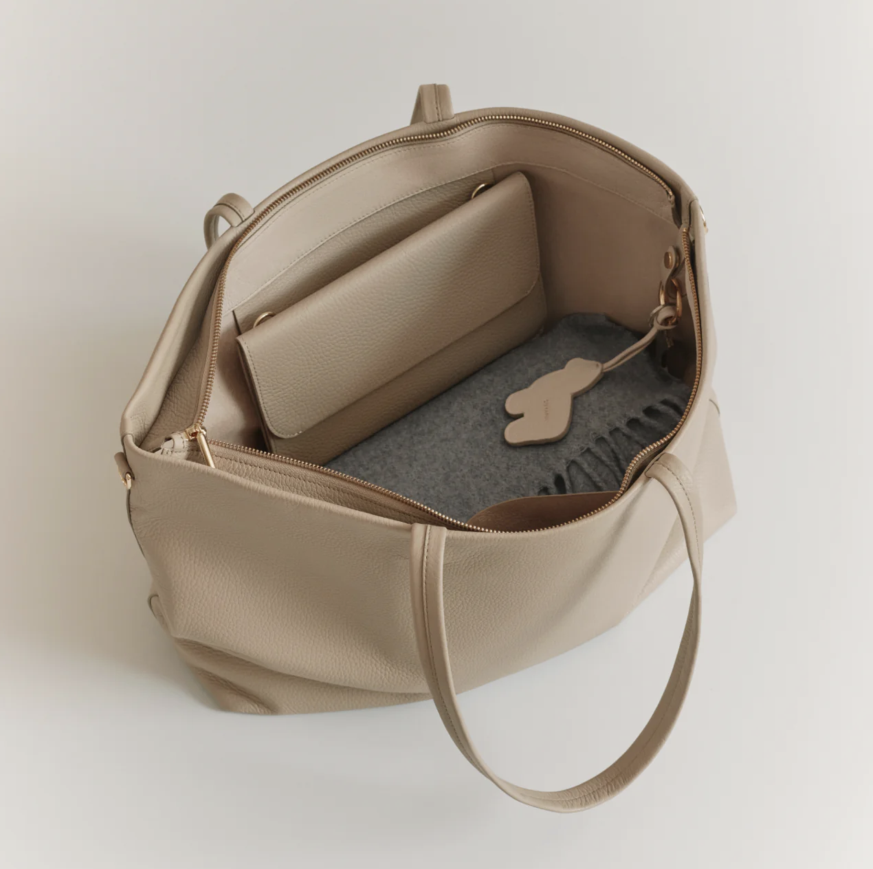 Open beige leather handbag with a padded pocket, gray felt lining, and a Bunny-shaped keychain inside.