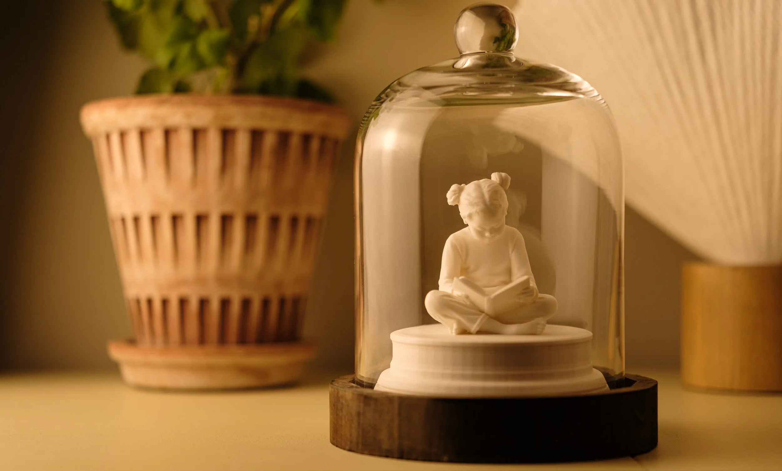 En prydnadsfigur av en liten flicka som sitter och läser bok, placerad under en glaskupa.