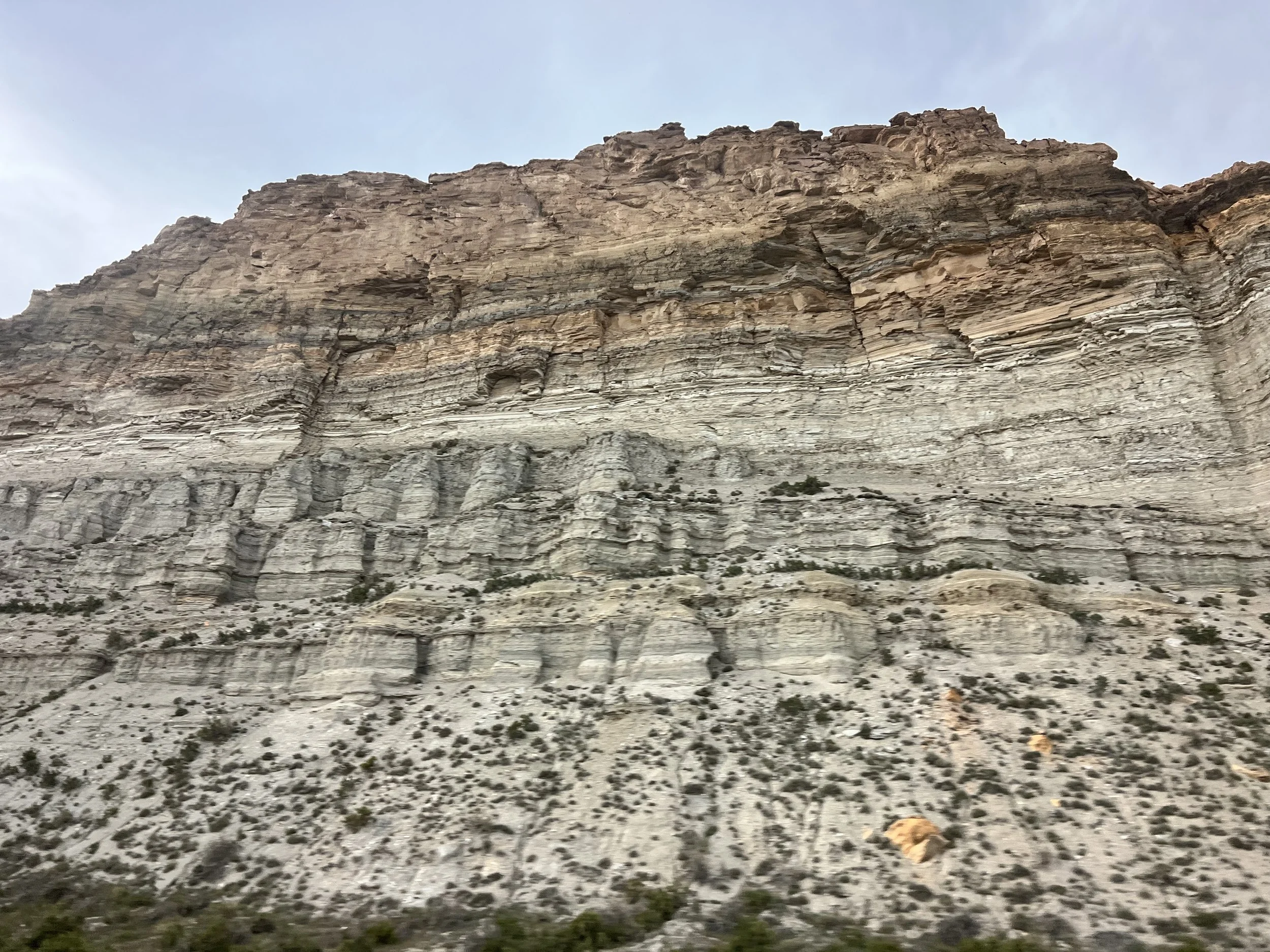 A large rocky mountain with layered sedimentary rocks and sparse vegetation at the base.
