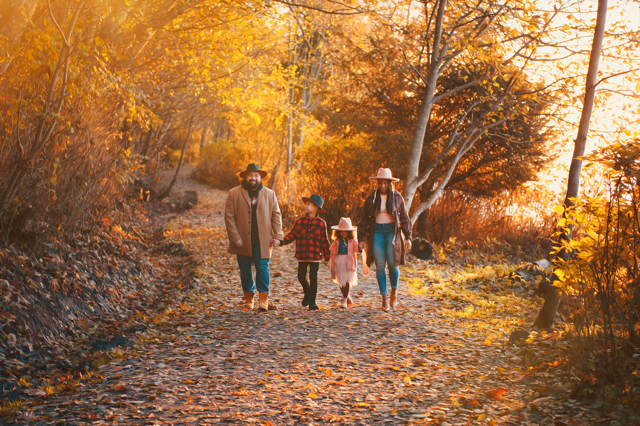 Family of four walking on a leaf-covered trail in autumn with trees in fall colors