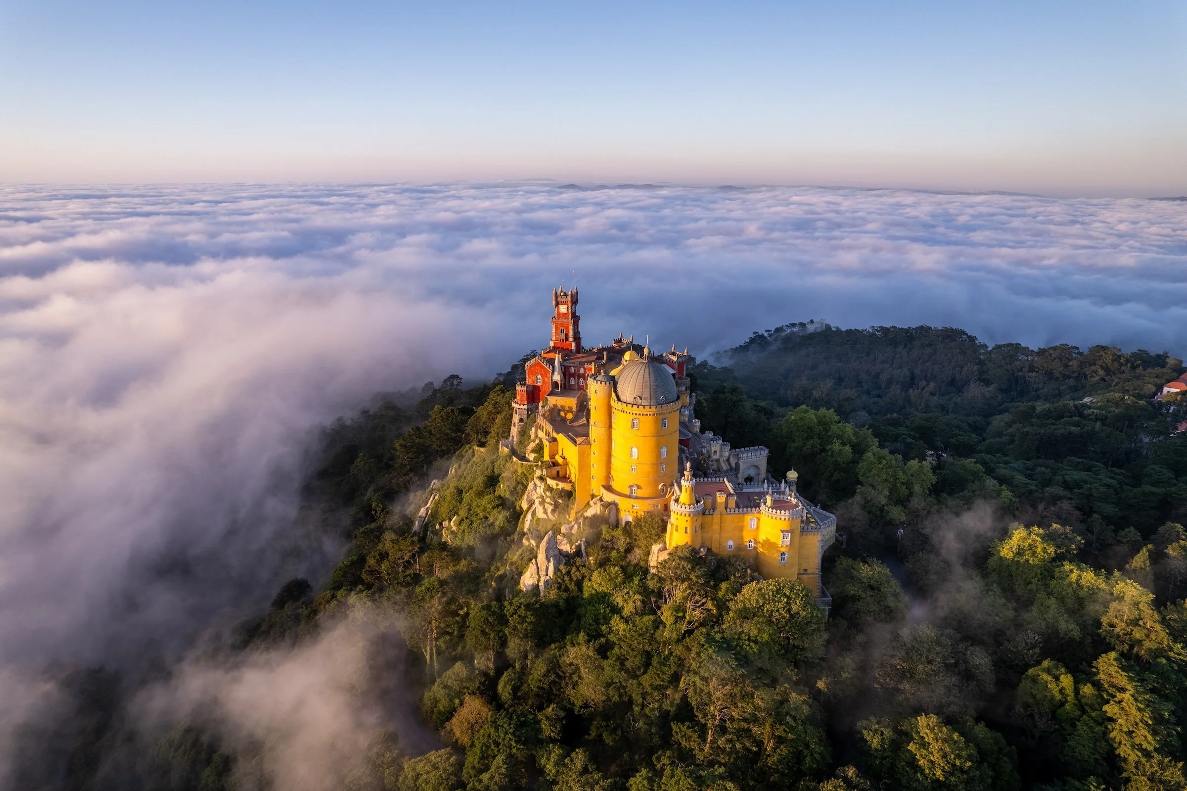 Pena Palace in Sintra, Portugal, perched on a foggy hilltop with a cloud-filled sky in the background.