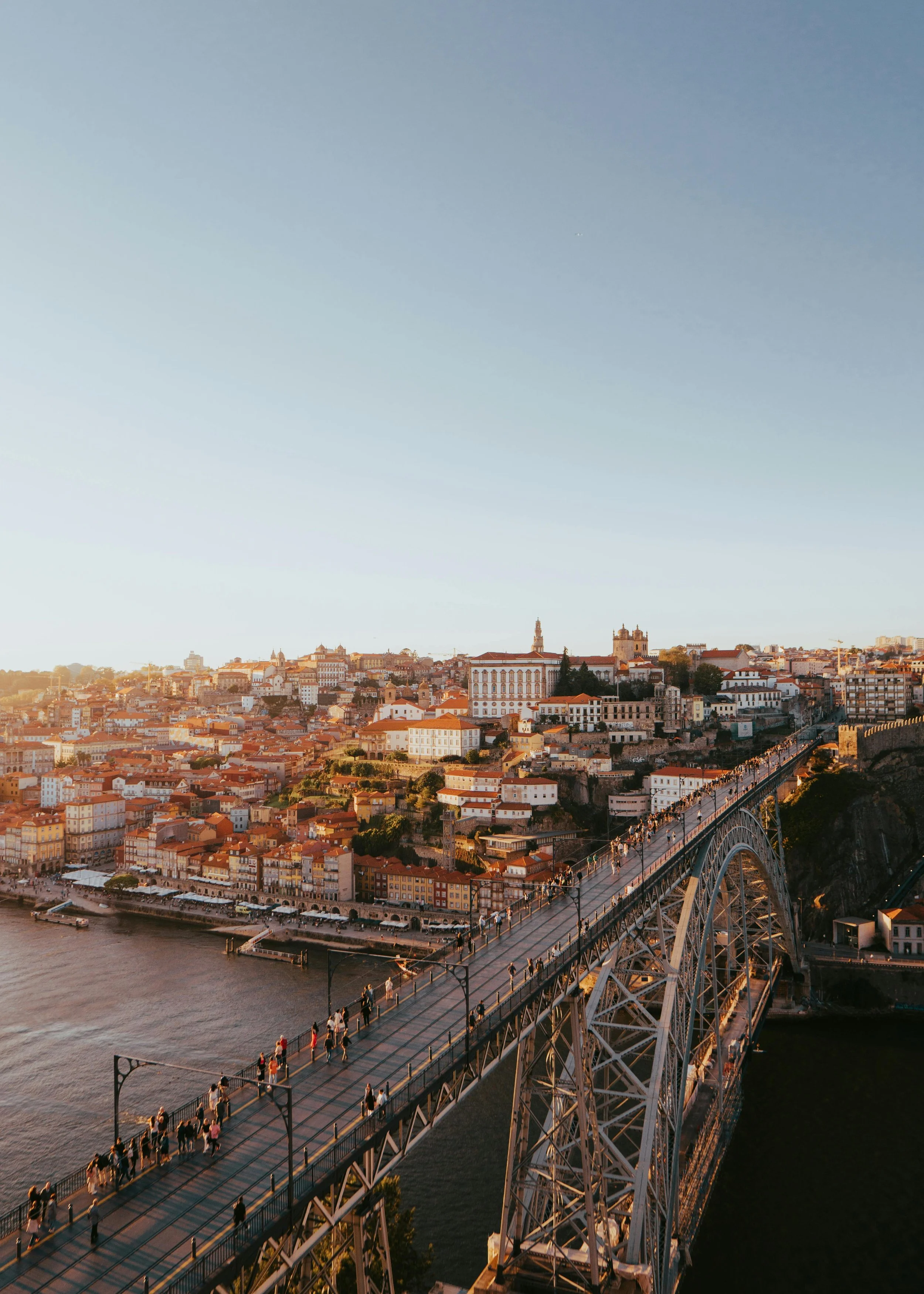Aerial view of Dom Luís I Bridge over the city of Porto, Portugal, during sunset with pedestrians walking on the bridge and colorful buildings along the riverbank.