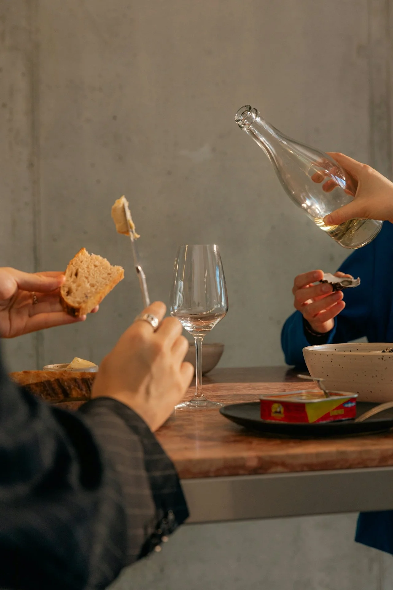 A group of people at a dinner table enjoying bread, wine, and snacks with a rustic background.