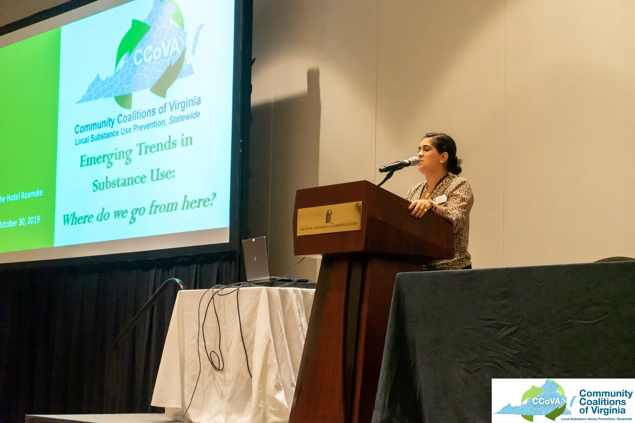 Female presenter at lectern with projector screen in background
