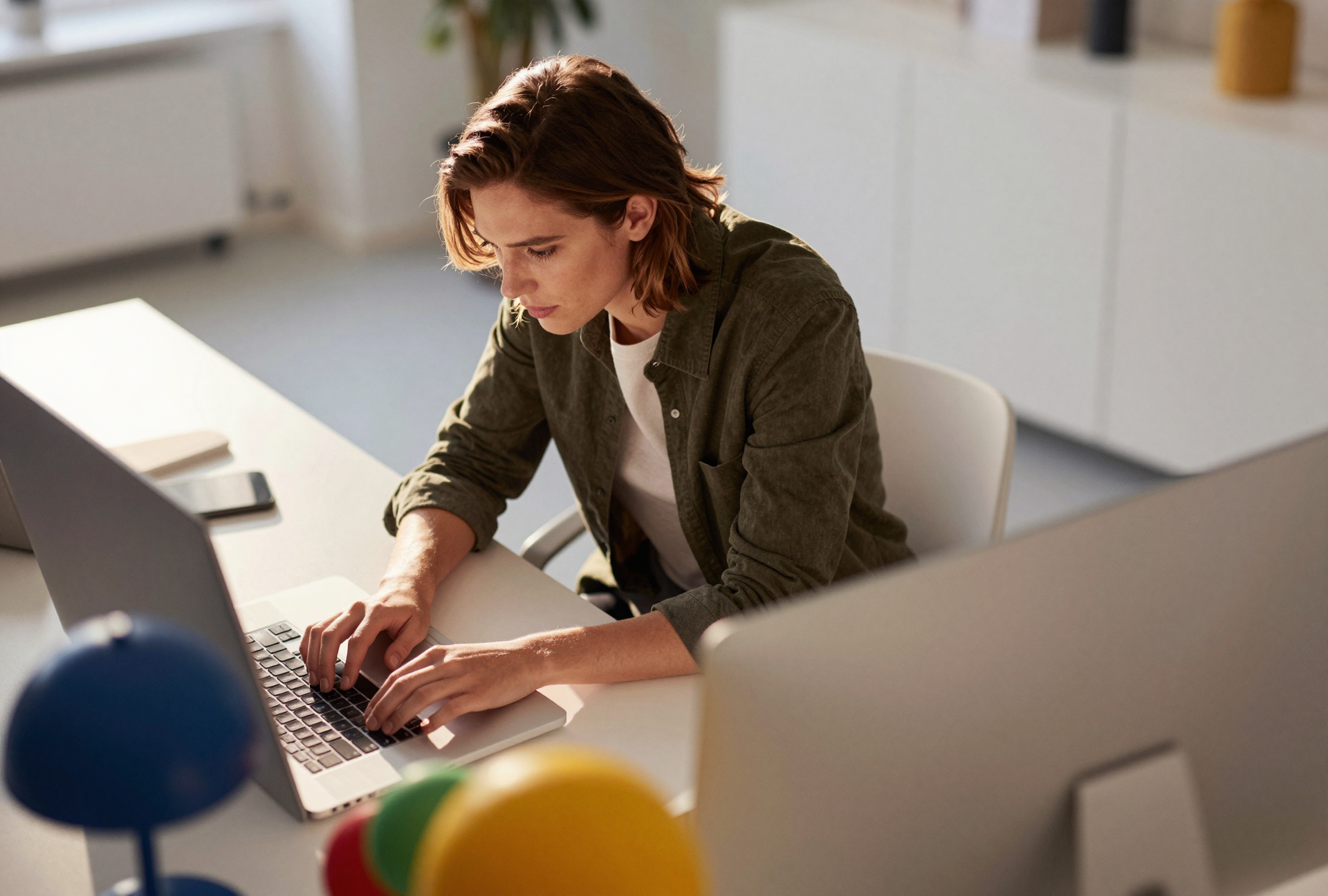 Woman with short brown hair working on a laptop at a desk in an office.