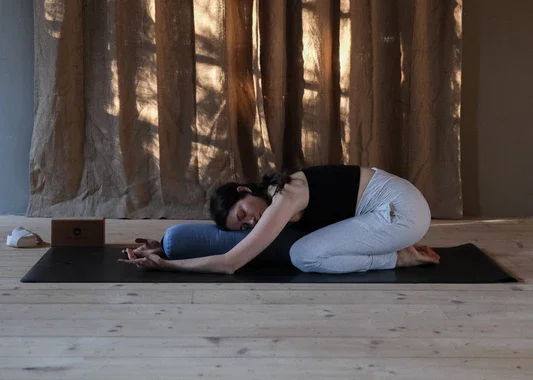 A practitioner rests in Child’s Pose, arms extended and breath steady — a quiet moment of reset within a softly lit studio space.