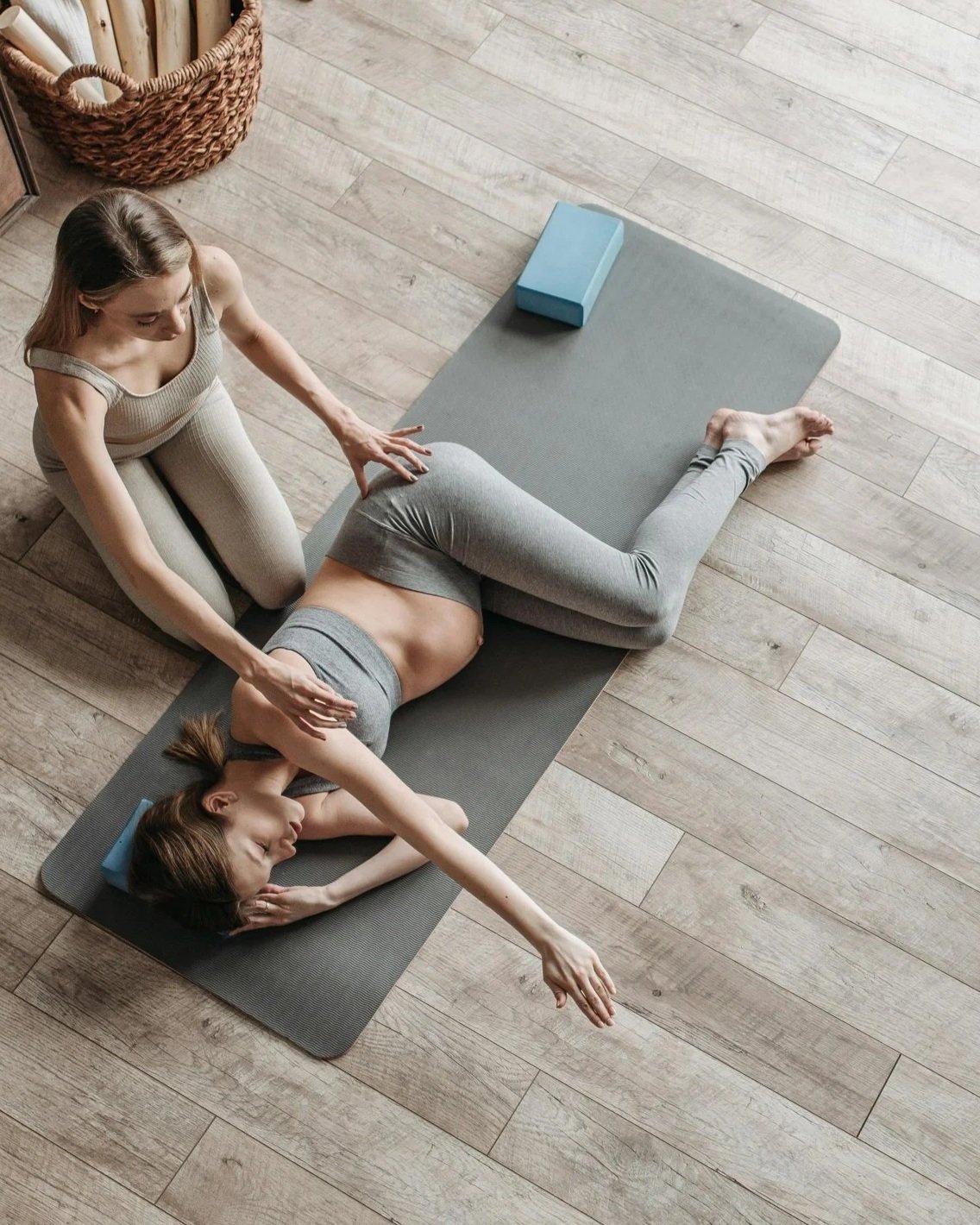 A prenatal practitioner receives supportive guidance in a grounded stretch, using props to create comfort, strength, and steadiness during pregnancy.