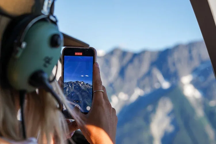 Passenger photographing mountain scenery during helicopter flight.