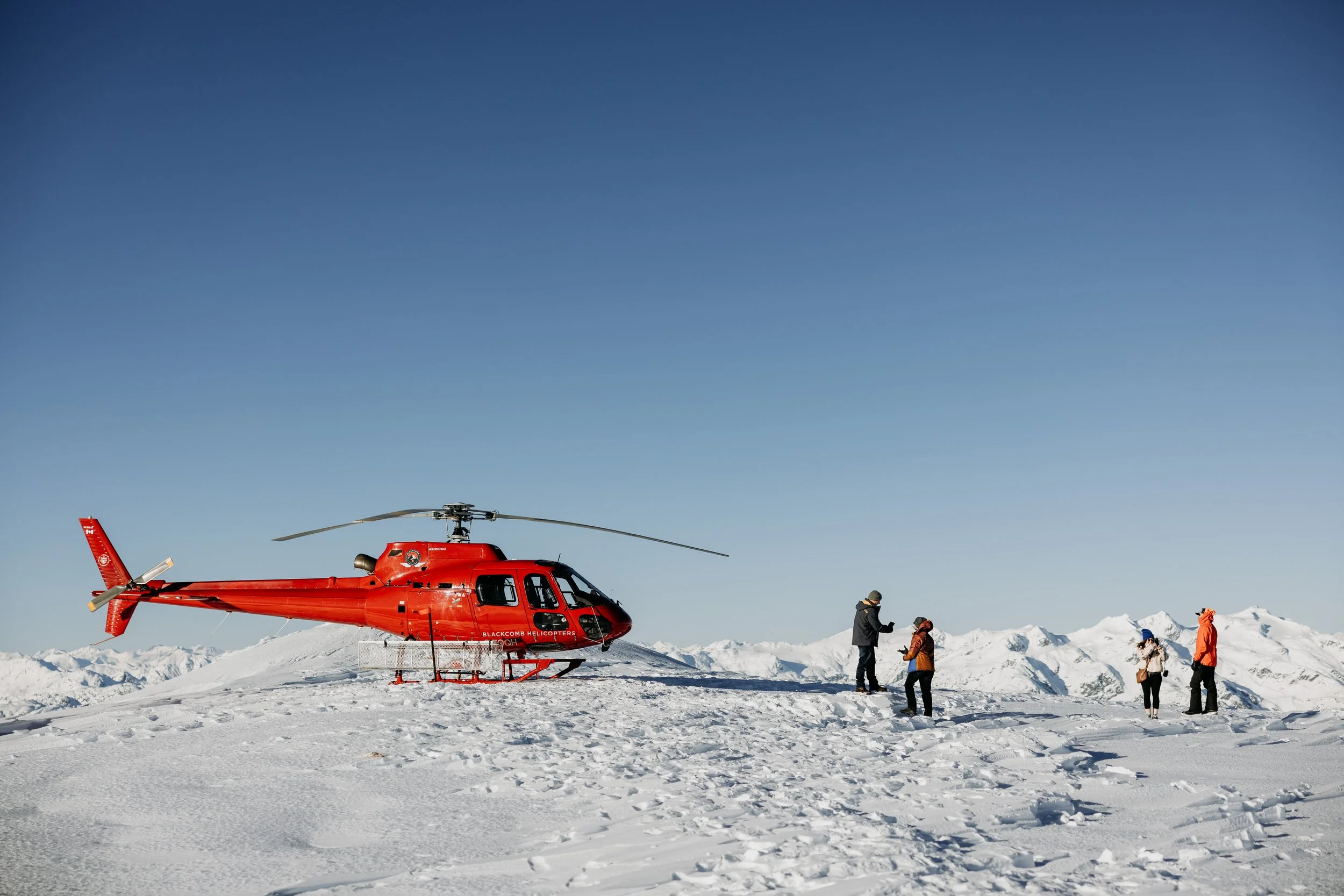 Red sightseeing helicopter landed on a snow-covered mountain top.
