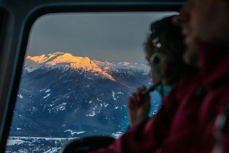 Passenger watching sunset over snow-covered mountains.