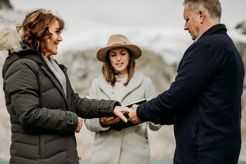 A woman and a man holding hands, with a young girl observing between them outdoors in a cloudy, mountainous setting.