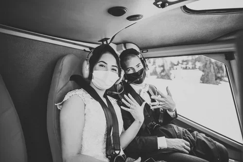 Two women sitting in a vehicle, wearing face masks and making peace signs with their hands.
